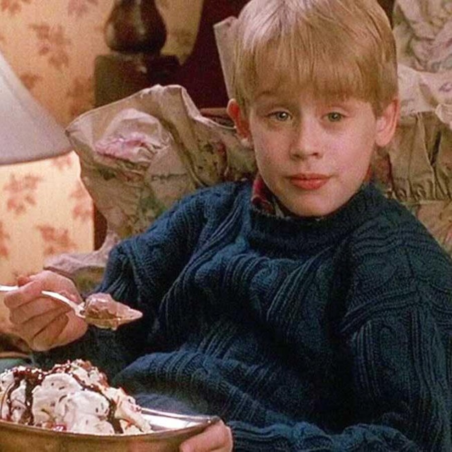 Un petit garçon en train de déguster un gros bol de crème glacée dans un lit de chambre d'hôtel.