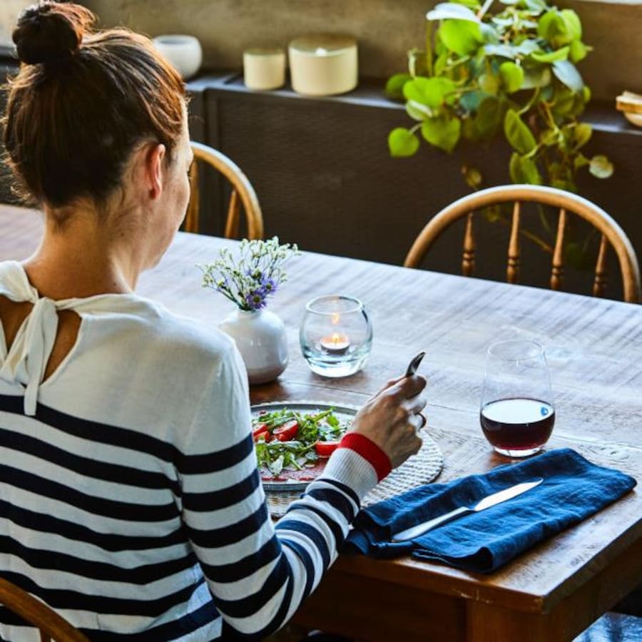 Une femme est assise à table, devant une assiette de salade.