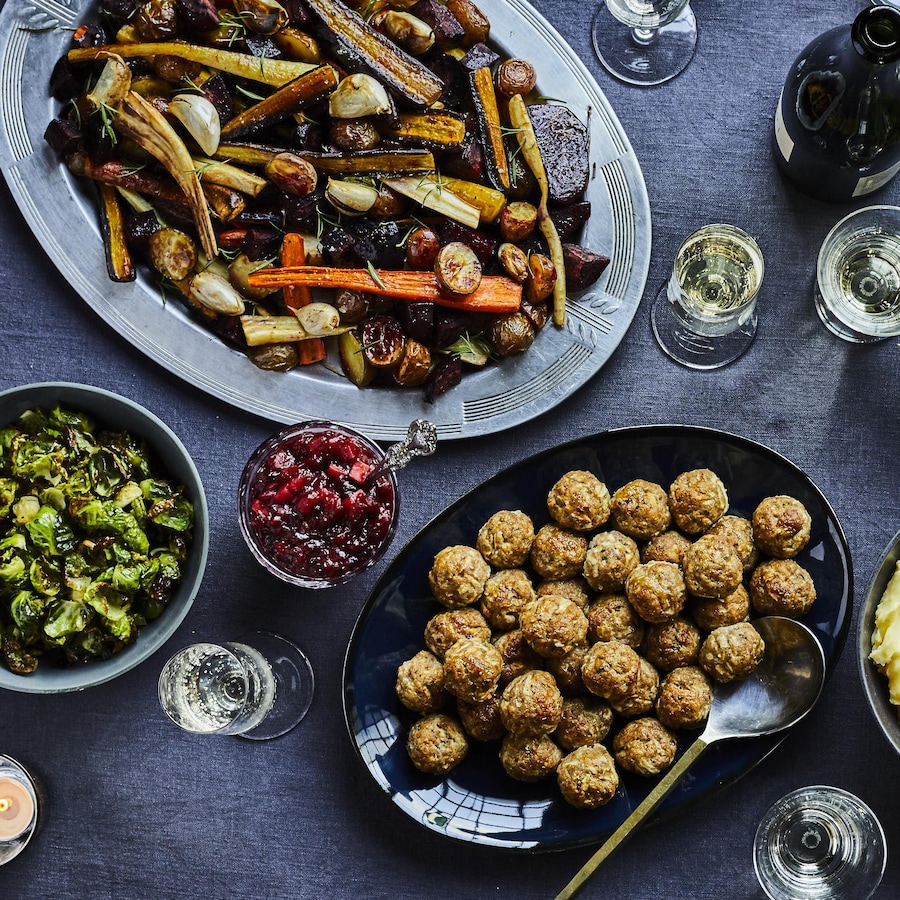 Table festive avec un plat de légumes rôtis, une salade verte, un plat de boulettes de viande et un bol de purée de pommes de terre.