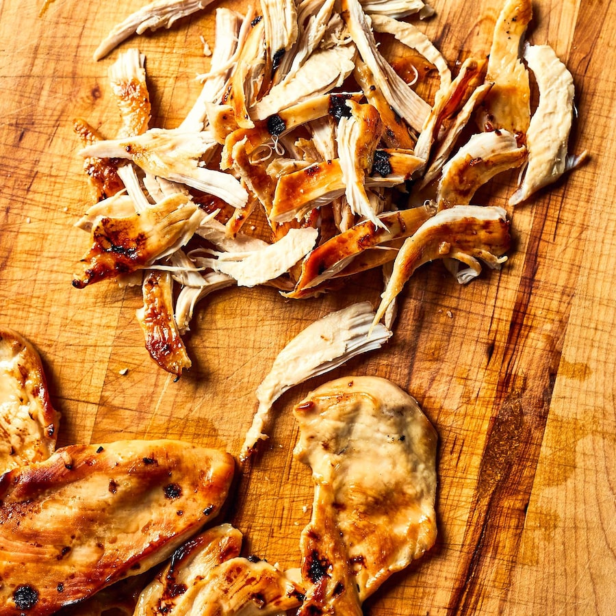 Poulet grillé effiloché sur une planche de bois.