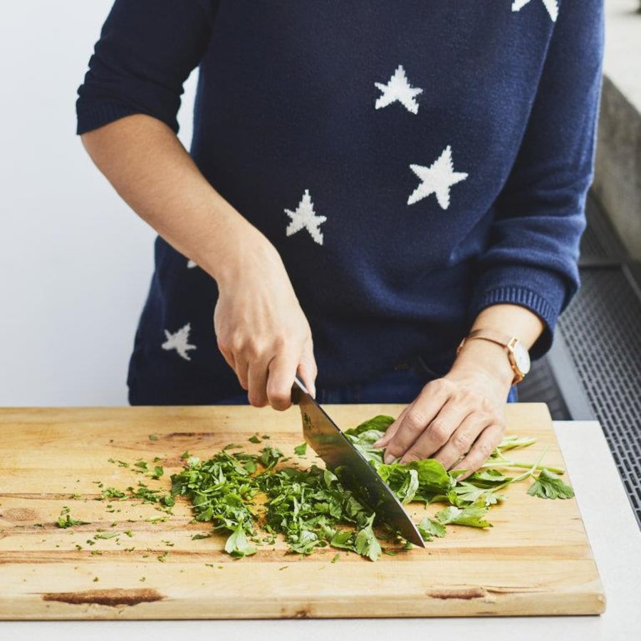 Une personne coupe du persil italien en utilisant un couteau de cuisine sur une planche à découper. 
