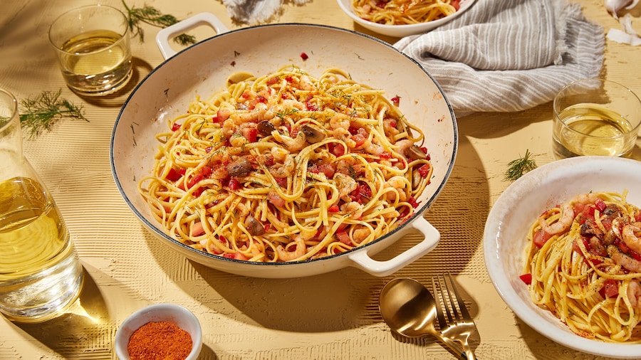 Un grand plat de linguinis aux fruits de mer et deux bols prêts à être dégustés.