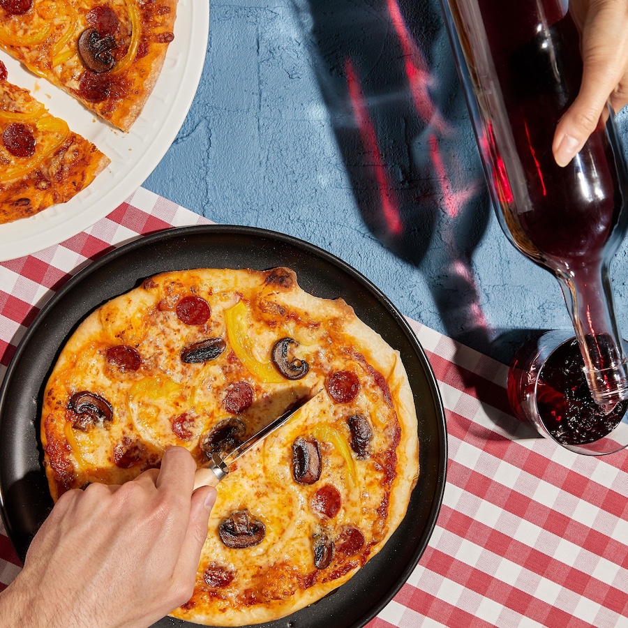 Deux pizzas garnies de pepperonis et de champignons avec des verres de vin rouge.