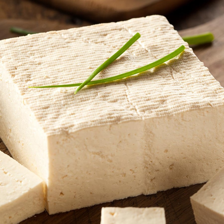 Un bloc de tofu coupé en morceaux sur une planche à découper.