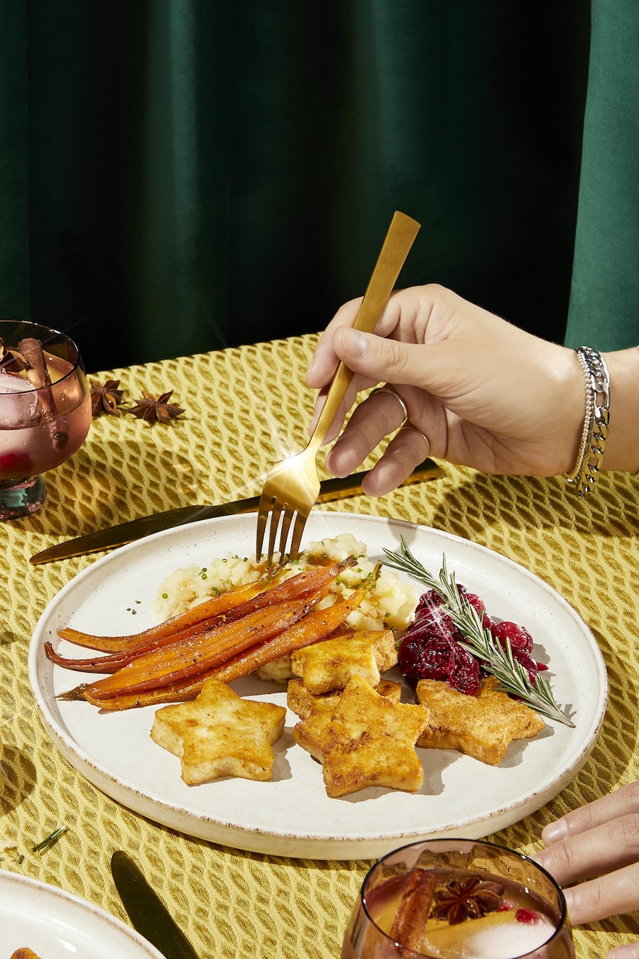 Une table des fêtes avec une assiette de tofu, carottes glacées, purée de pomme de terre et compote de canneberges.