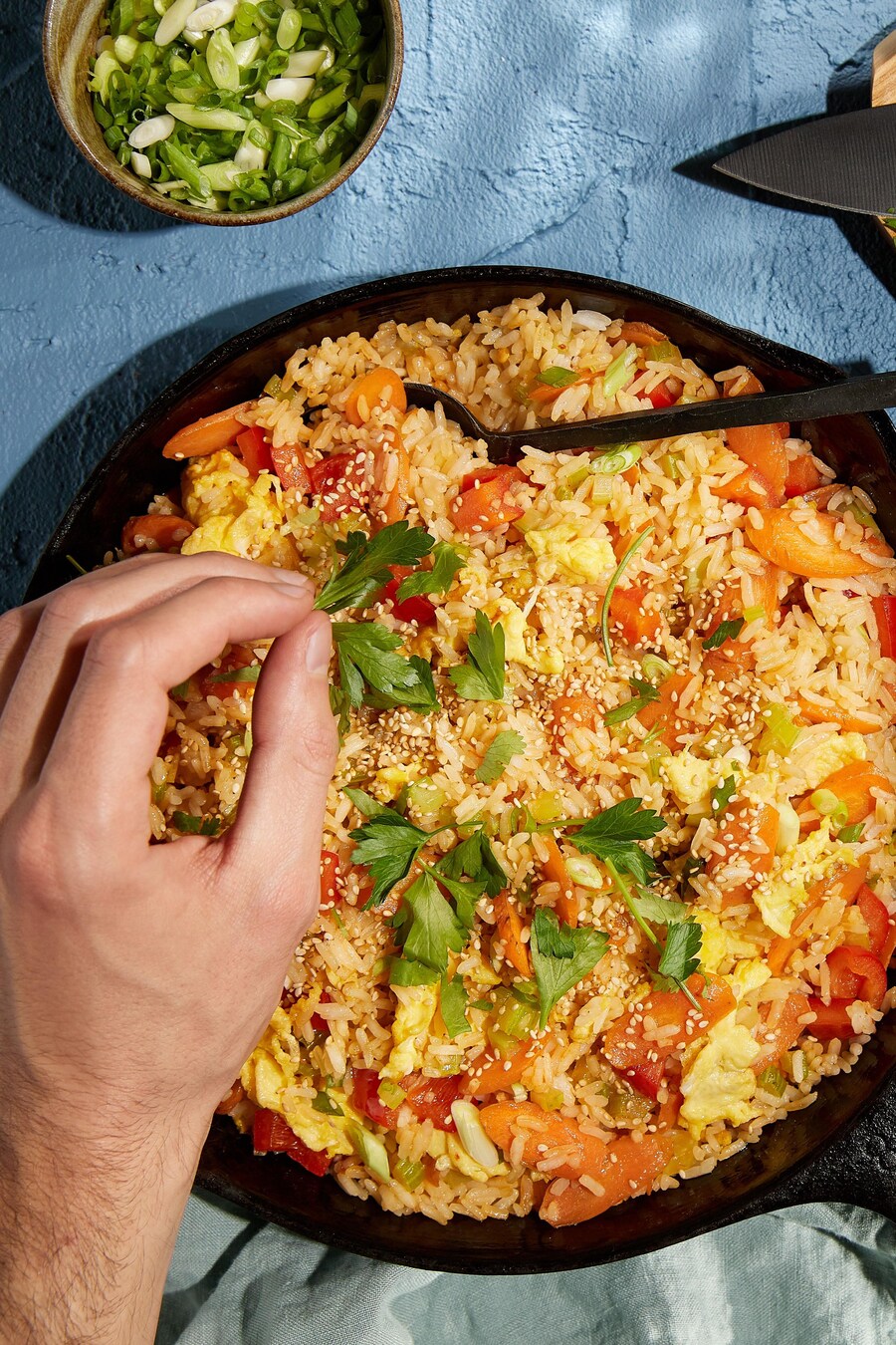 Une poêle remplie de riz frit avec des légumes, de la coriandre et des graines de sésame.