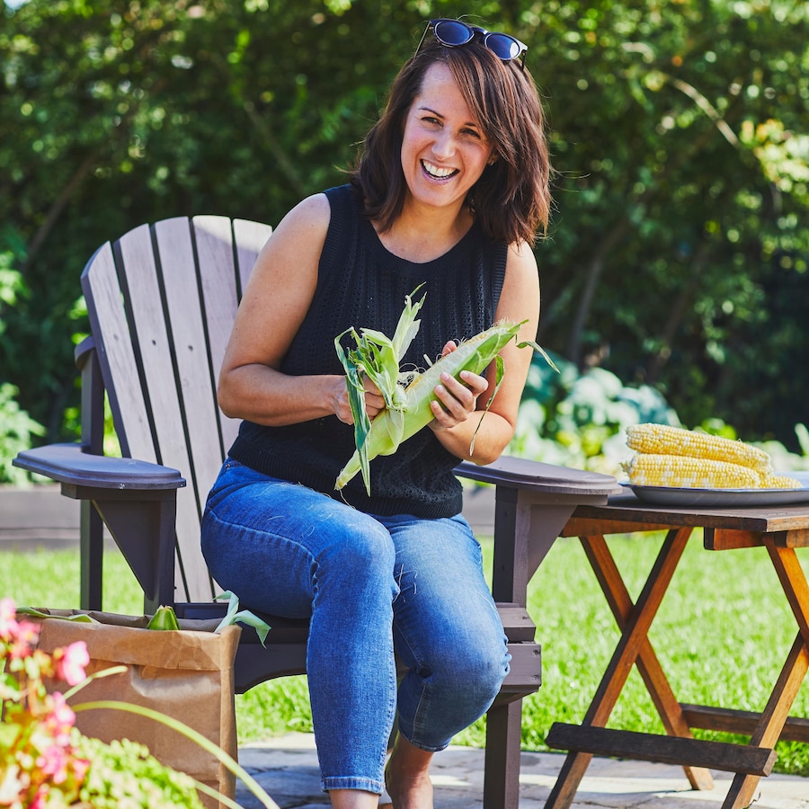 La nutritionniste Geneviève O'Gleman est assise sur une chaise à l'extérieur et elle épluche du maïs.
