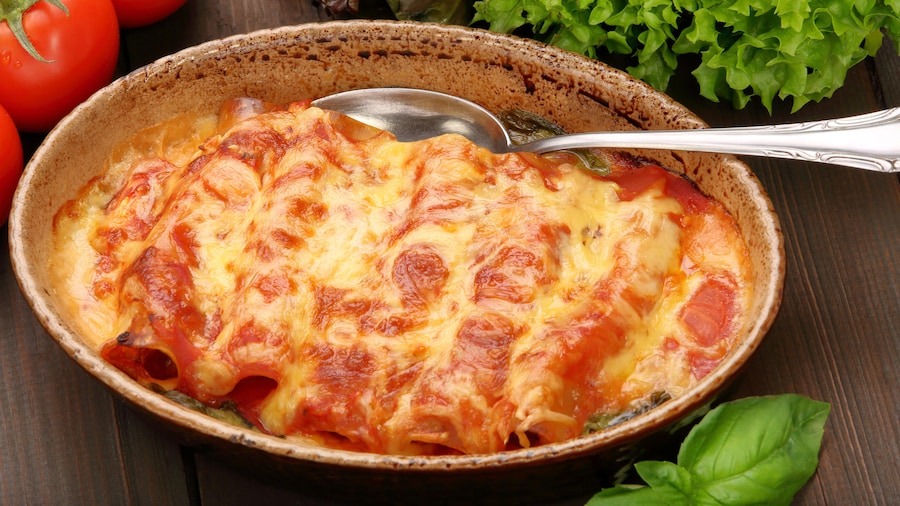 Dans un plat ovale, il y a des cannellonis farcis cuits dans de la sauce béchamel et de la sauce tomate.