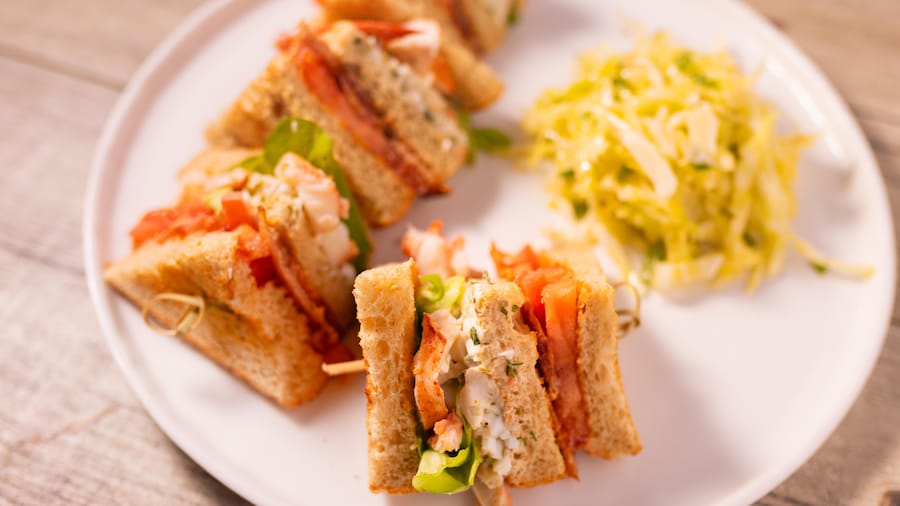 Un club sandwich au homard servi dans une assiette avec une salade d'accompagnement.