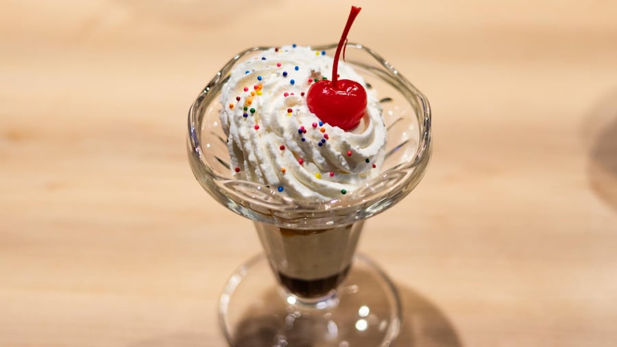 Une coupe remplie de crème glacée à la vanille et garnie de quelques bonbons et d'une cerise.