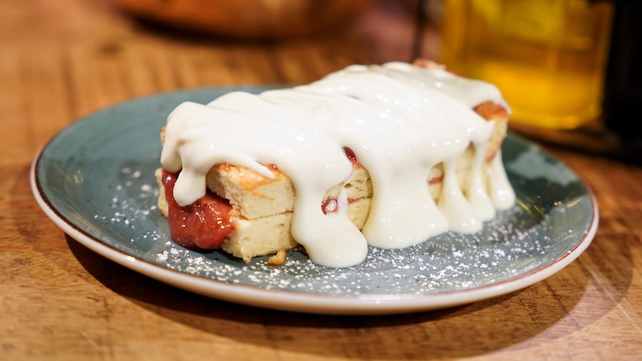 Une portion de gâteau éponge dans une assiette avec de la compote de rhubarbe et fraise et de la crème.