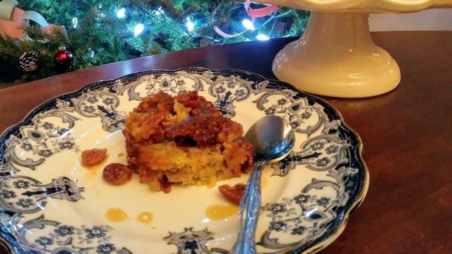Un morceau de gâteau aux fruits dans une assiette avec un arbre de Noël en arrière plan.