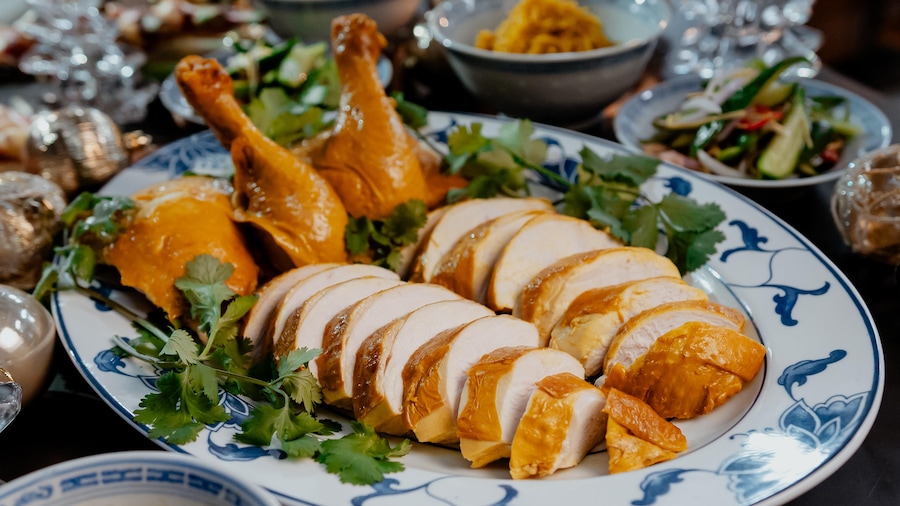 Un poulet poché découpé en tranches dans un plat de service, avec de la coriandre fraîche.