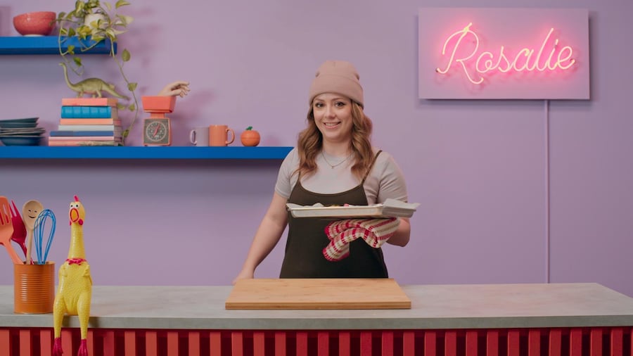 Rosalie tient dans sa main une plaque de cuisson contenant les poitrines de poulet. 