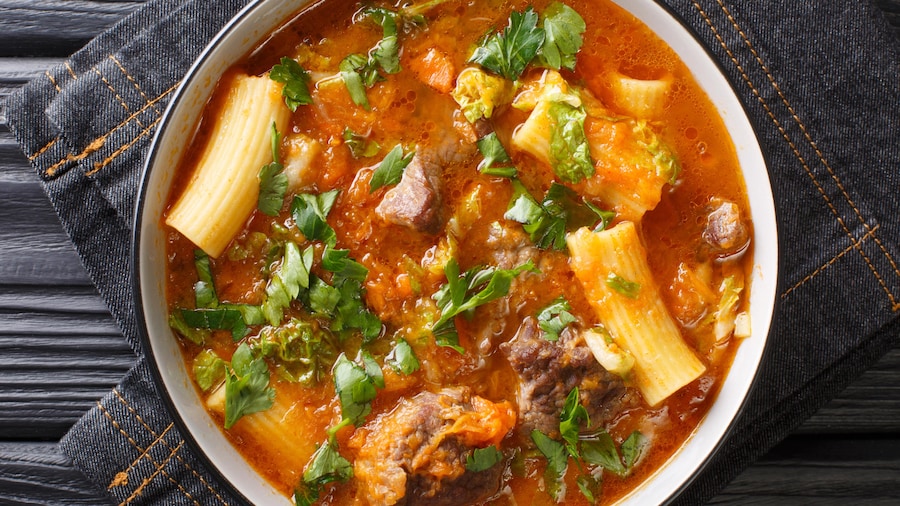 Un bol de soupe joumou, avec un bouillon aux tomates, des pâtes et de la viande.
