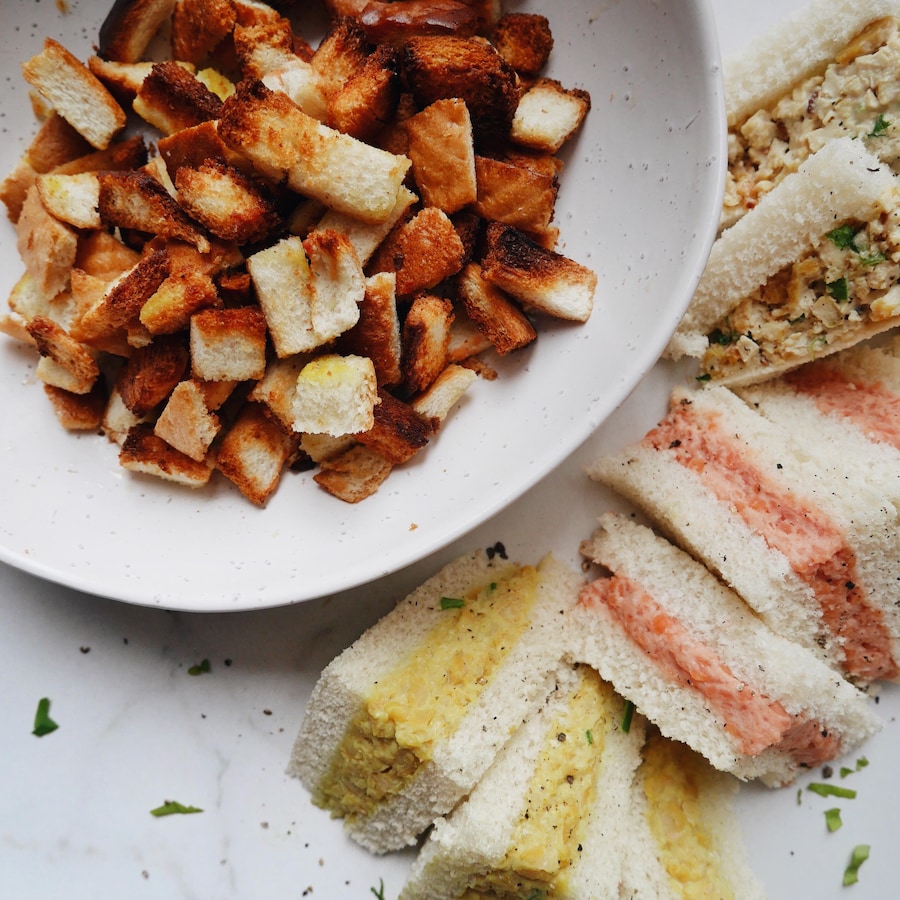 Des croûtons de pain disposés dans une assiette. Autour de l'assiette se trouvent des sandwichs sans croûte.