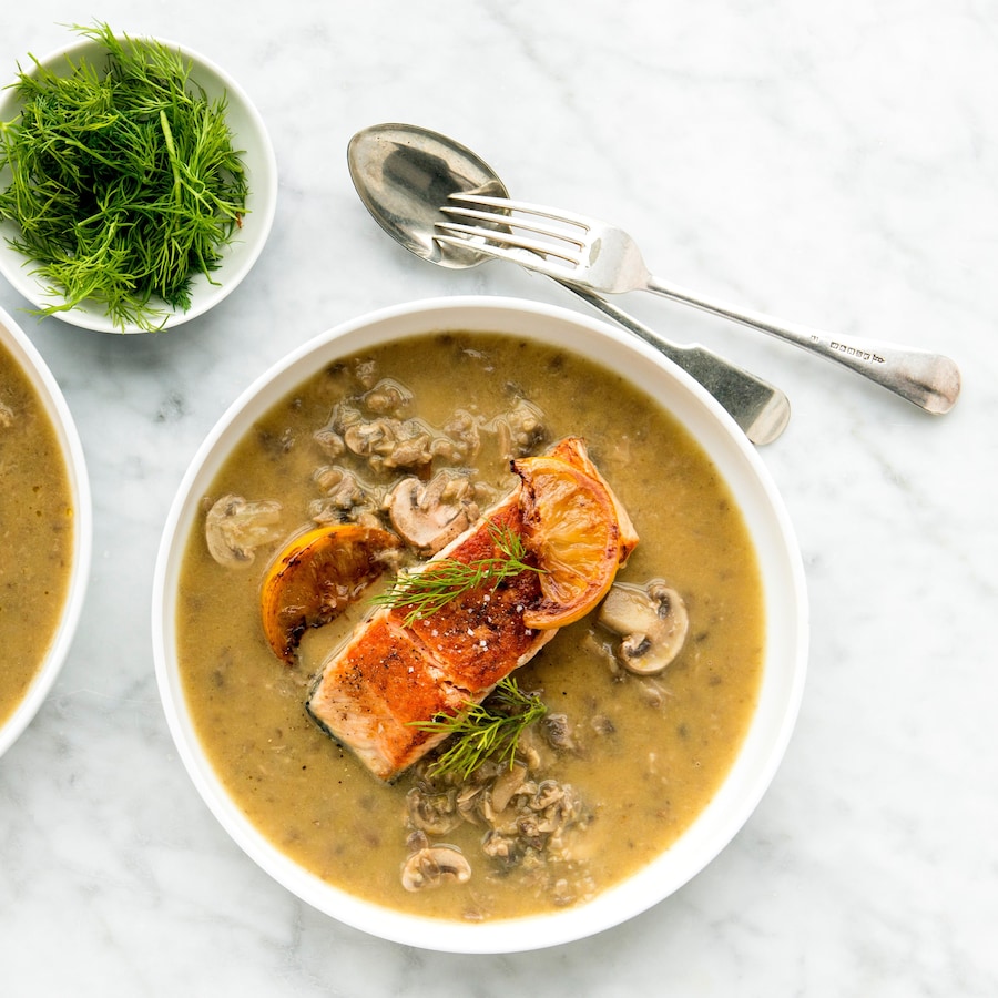 Deux bols de soupe remplis de soupe veloutée aux champignons avec du saumon poêlé sur le dessus.