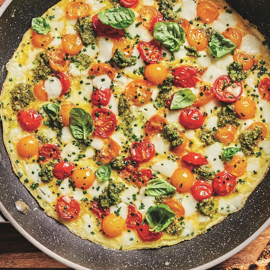 Une omelette aux tomates, mozzarella et pesto dans une poêle.