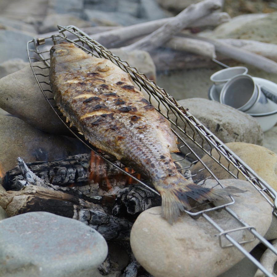 Un poisson entier dans une grille à poisson, au-dessus d'un feu de camp.