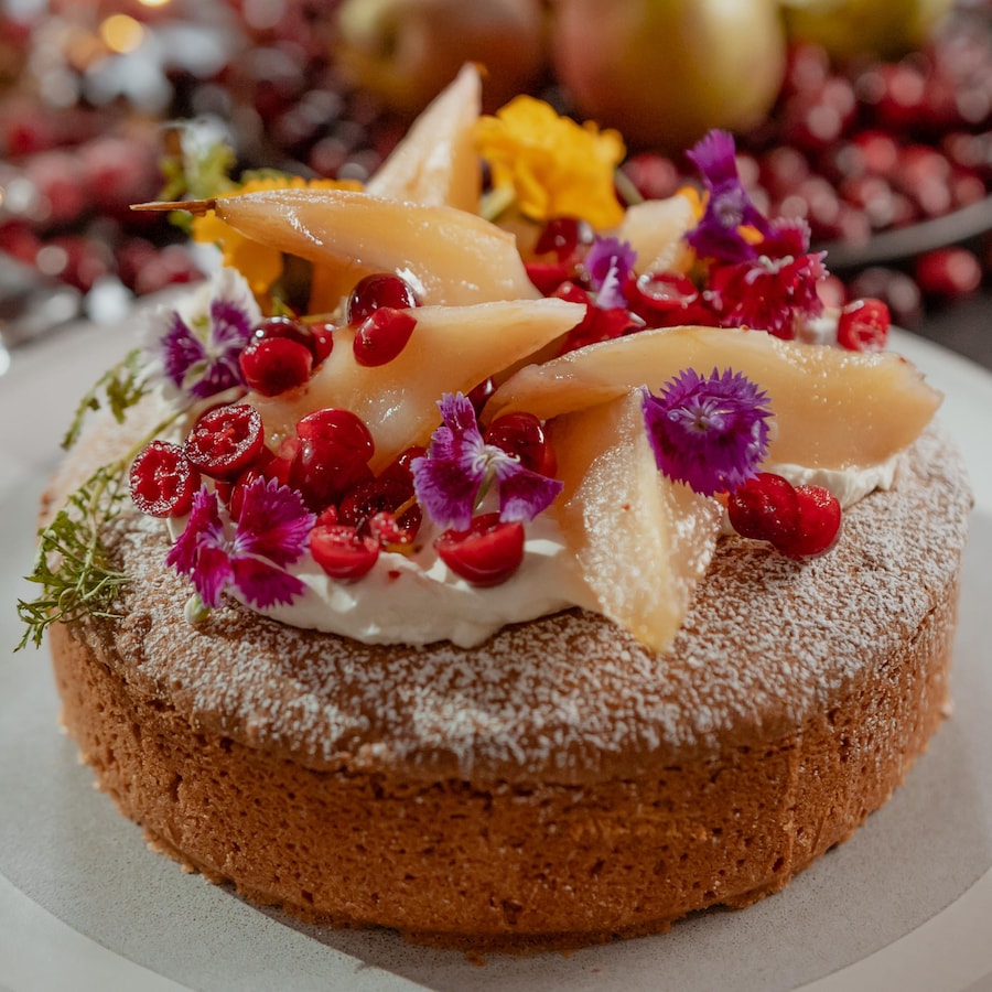 Un gâteau recouvert de poires, de canneberges et de fleurs comestibles.
