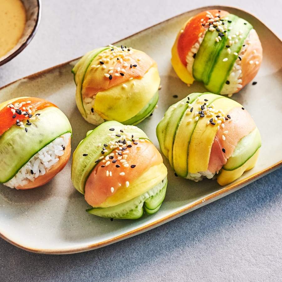 Des boules de riz à sushi garnies de tranches de légumes servies avec de la sauce au sésame.