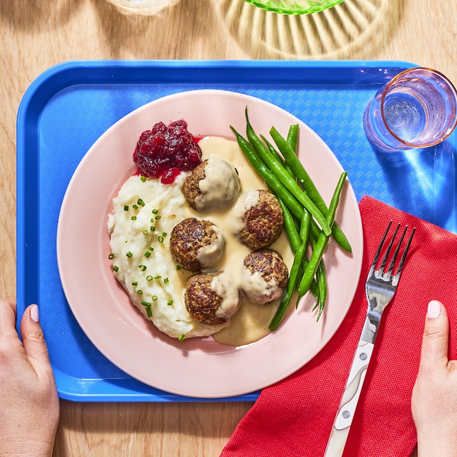 Un plateau de cafétéria avec une assiette contenant de la purée de pommes de terre, des boulettes suédoises et des haricots verts.