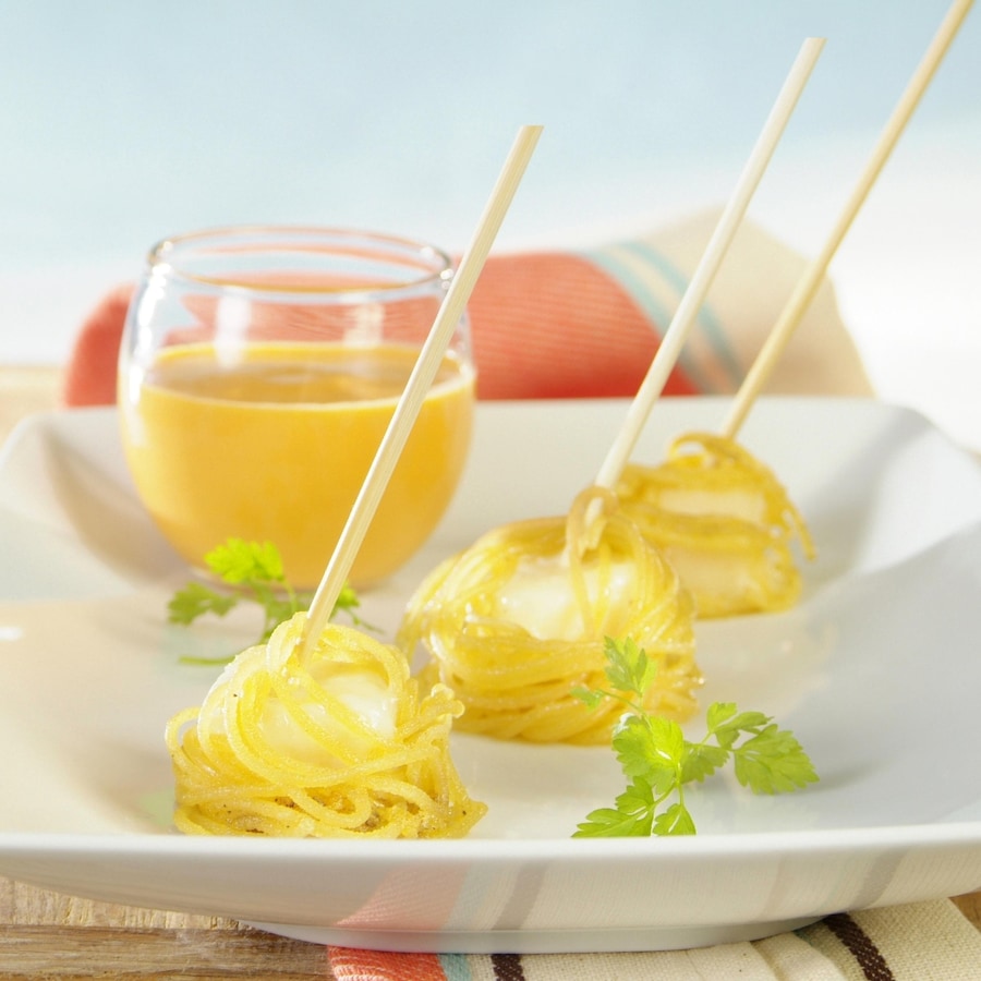 Trois fondues parmesan enveloppés de spaghettis disposés dans une assiette blanche aux côtés d'un verre à cocktail de coulis jaune.