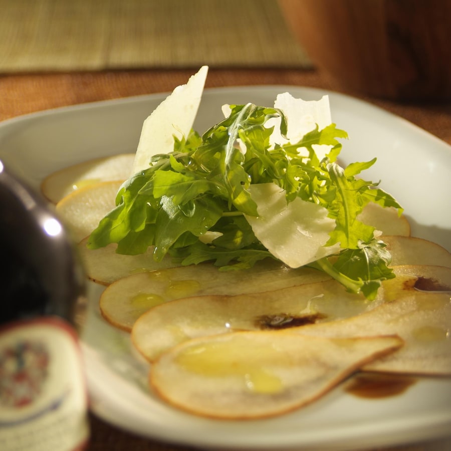 Carpaccio de poires bosc, salade de roquette dans une assiette.