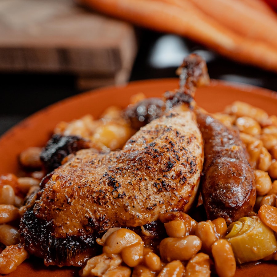 Une assiette contenant des haricots, une saucisse et du poulet.