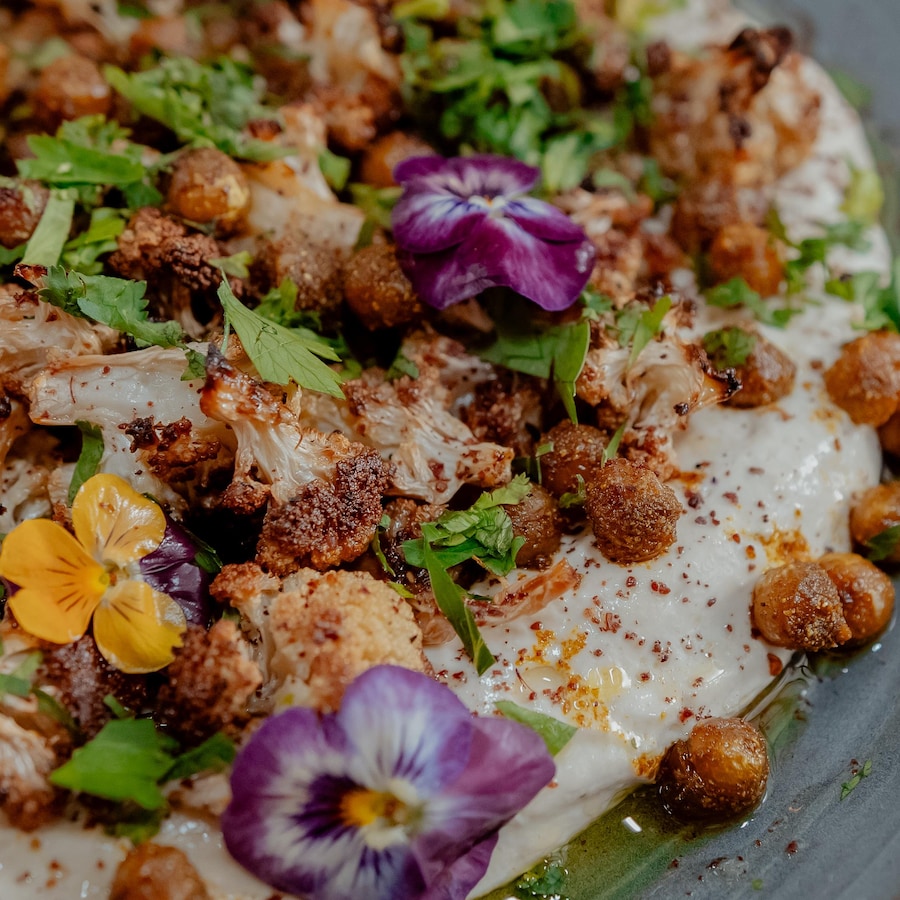 Une assiette de yogourt garni de chou-fleur rôti, de pois chiches croustillants, de fleurs comestibles et de fines herbes.