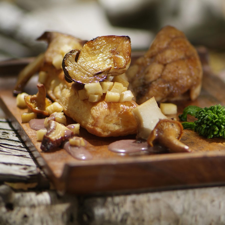 Ris de veau cuits décorés de champignons sauvages rôtis dans une assiette en bois.
