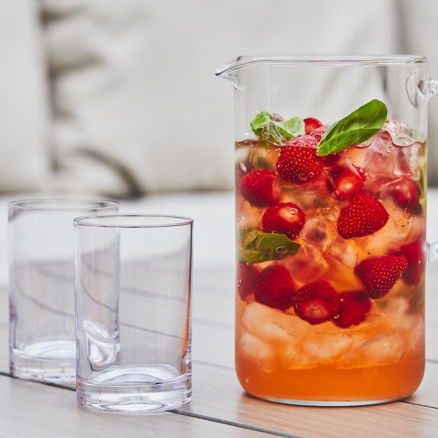 Un pichet transparent avec de l'eau fruitée aux fraises et au basilic avec deux verres vides juste à côté. 