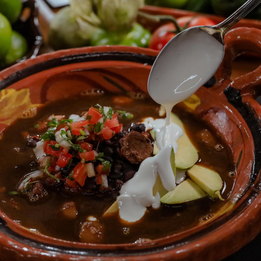 Une cocotte de frijoles charros avec une garniture de tomates et d'oignons en dés (pico de gallo)