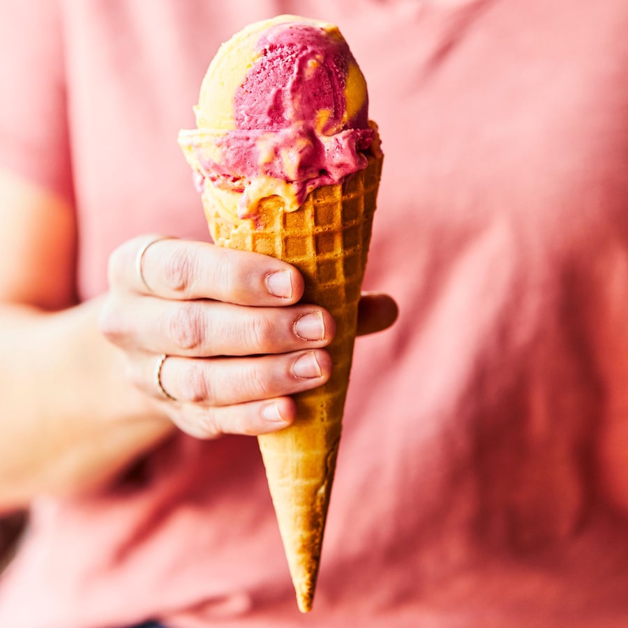 Une femme tenant dans sa main un cornet de crème glacée à la framboise et à la mangue.