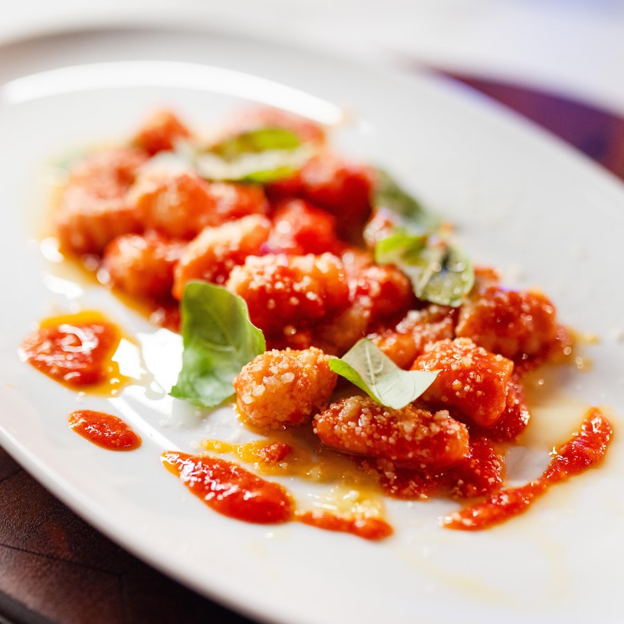 Des gnocchis à la sauce tomate servis avec du parmesan râpé et des feuilles de basilic.
