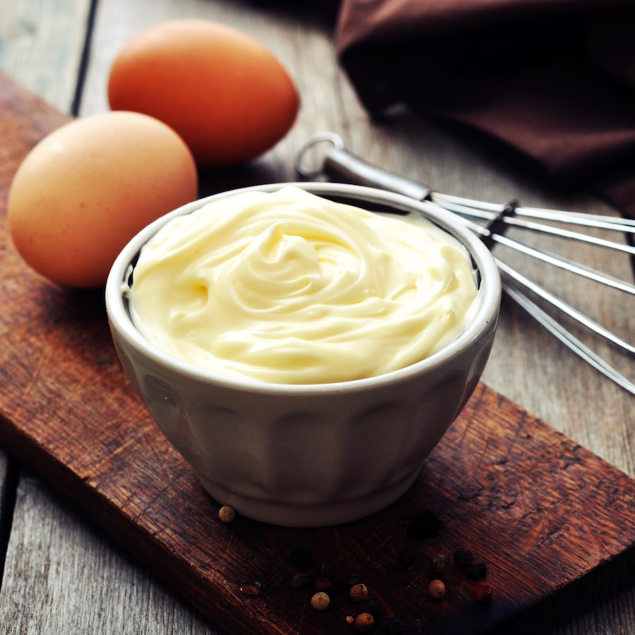 De la mayonnaise dans un bol avec des œufs à côté.