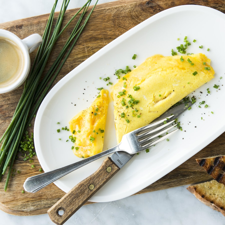Une assiette blanche avec une omelette française garnie de ciboulette vue de haut et accompagnée de rôties et d'une tasse de café.