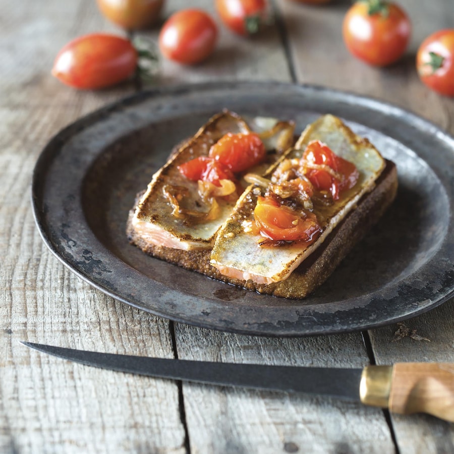 Deux petits filets de truite arc-en-ciel sur un morceau de pain avec un compoté de tomates cerises en garniture.