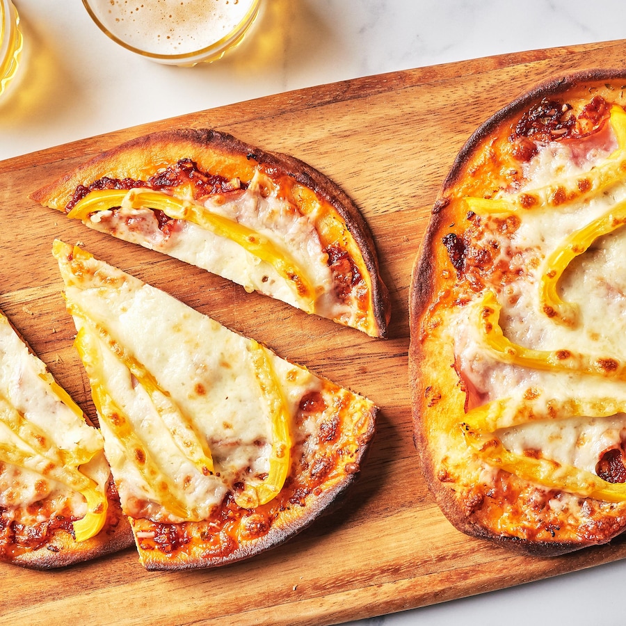 Des pizzas sur pains naans au capicollo et au poivron servies sur une planche de bois.
