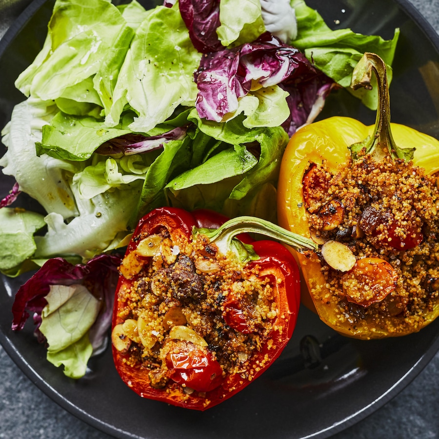 Deux poivrons farcis à la merguez et au couscous avec une salade verte dans une assiette. 