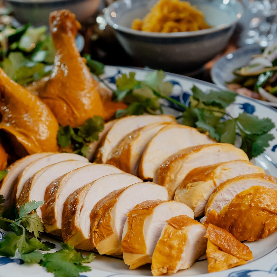 Un poulet poché découpé en tranches dans un plat de service, avec de la coriandre fraîche.