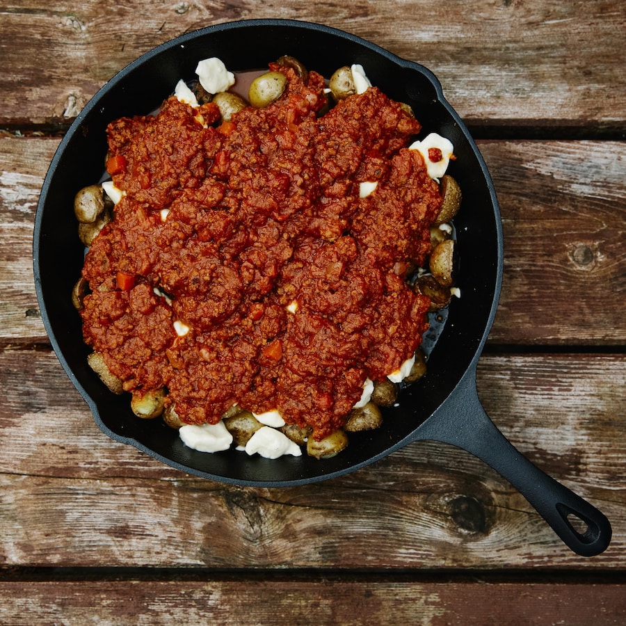 Sur une table en bois, est déposé une poêle rempli de poutine italienne.