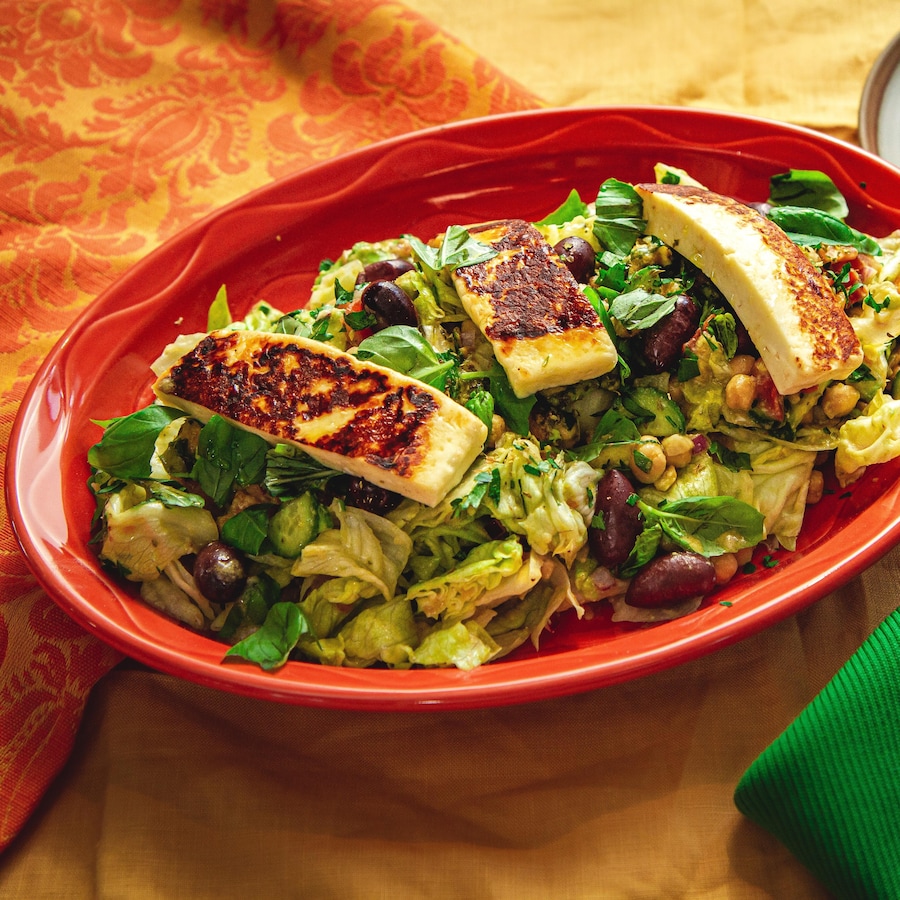 Une assiette de service remplie de salade méditerranéenne contenant des olives, de la laitue, des pois chiches et du fromage halloumi.