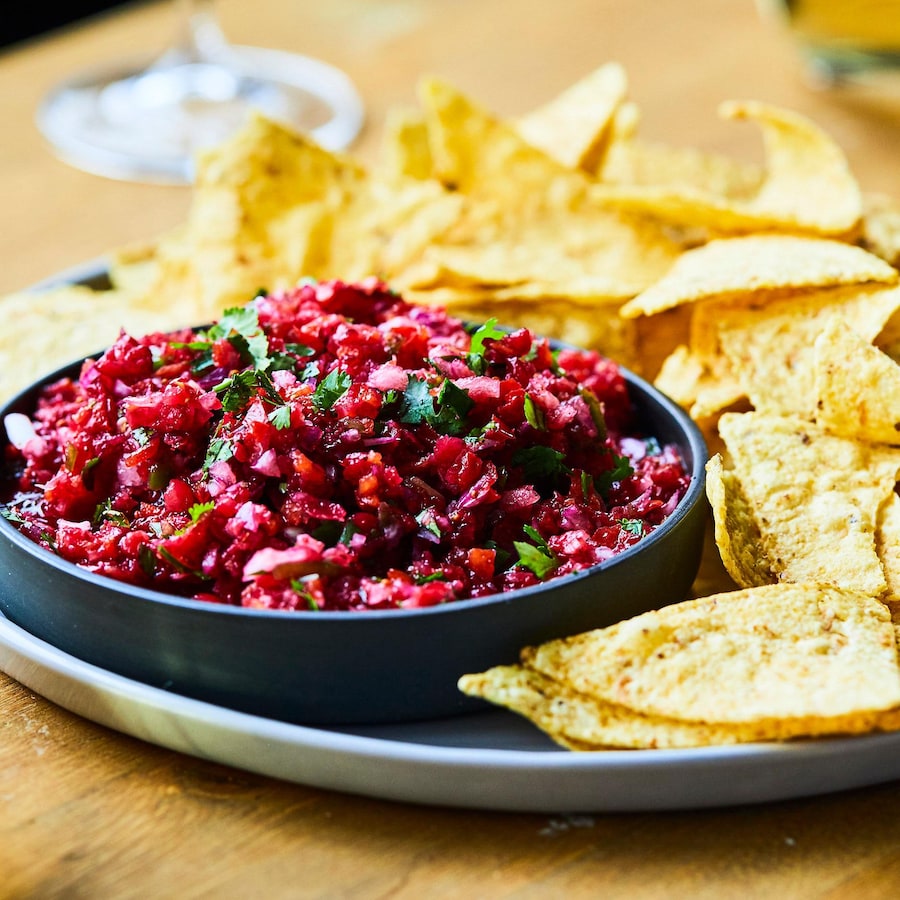 Salsa aux canneberges et à la coriandre dans un bol avec des croustilles de maïs dans une assiette.