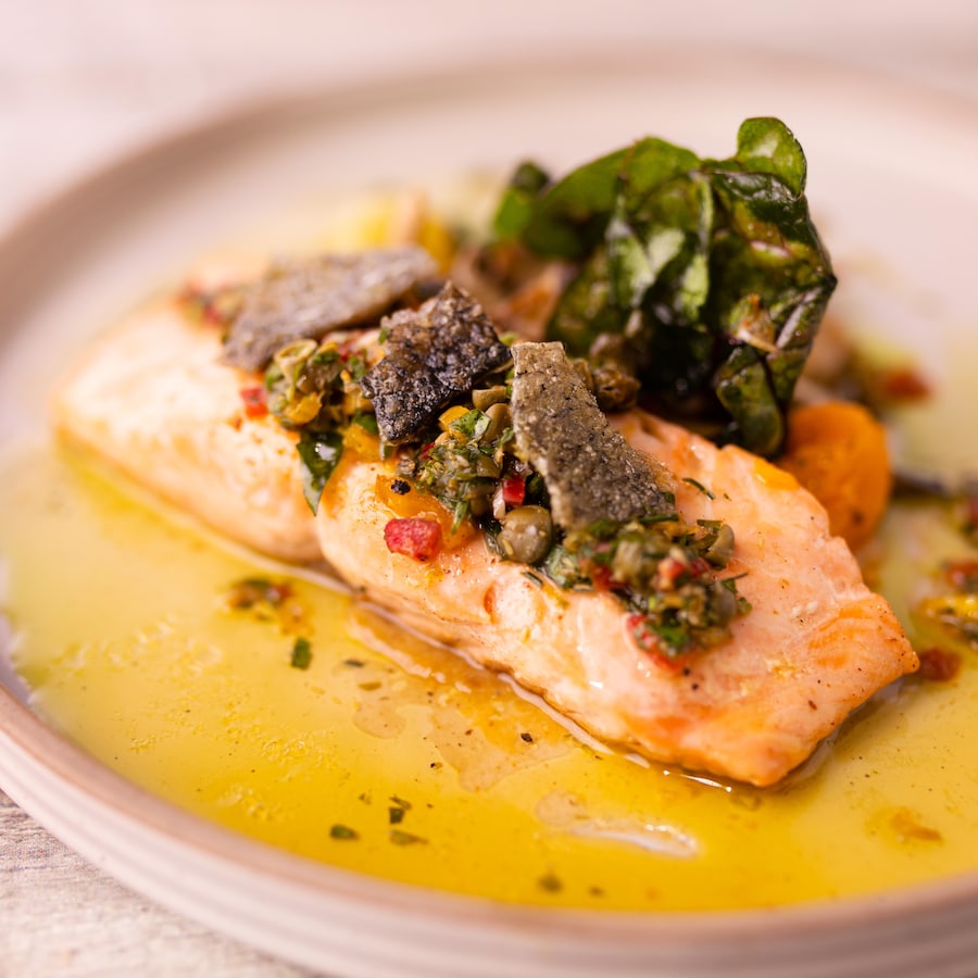 Un pavé de saumon garni de sauce et servi avec des légumes.