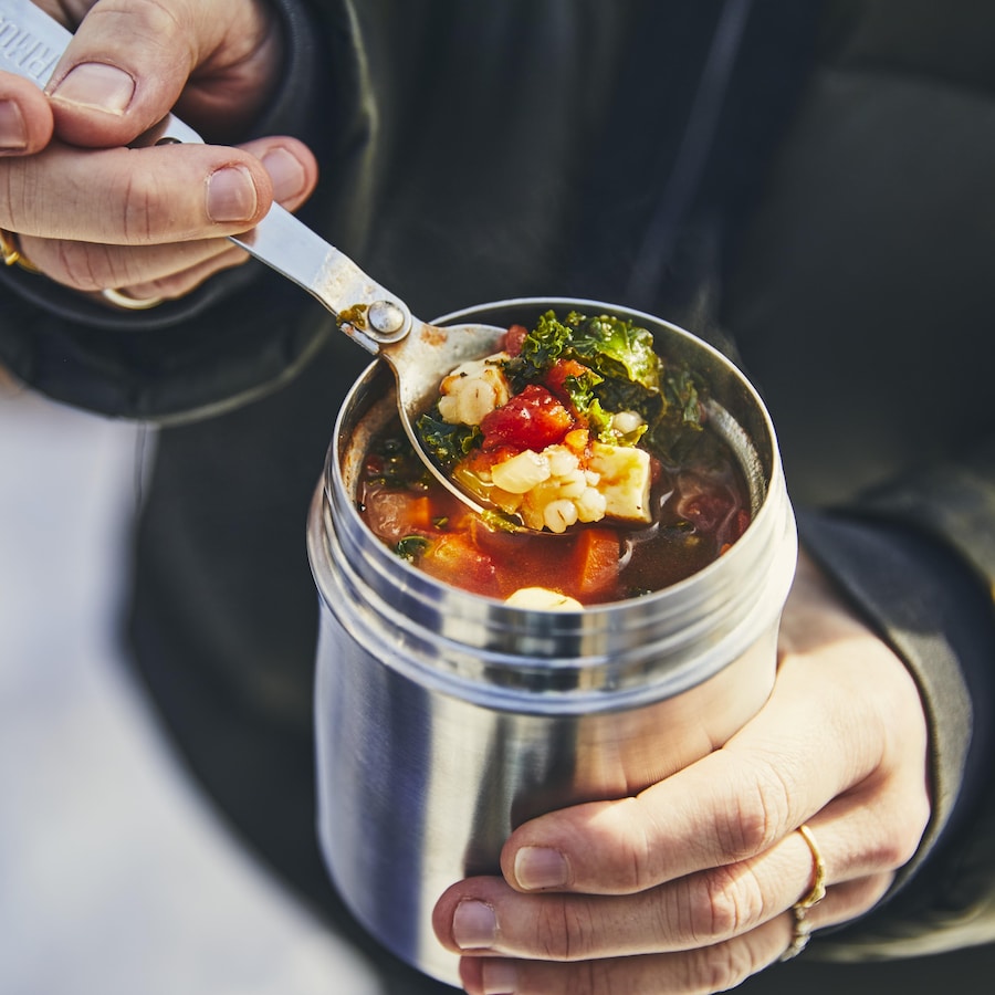 Une personne tient dans ses mains un thermos remplit de soupe.