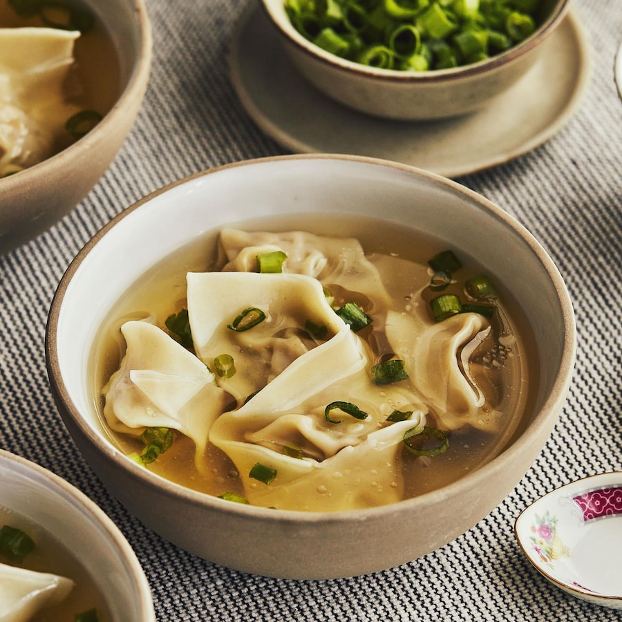 Un bol de soupe wonton avec des cuillères à soupe asiatiques et des oignons verts.