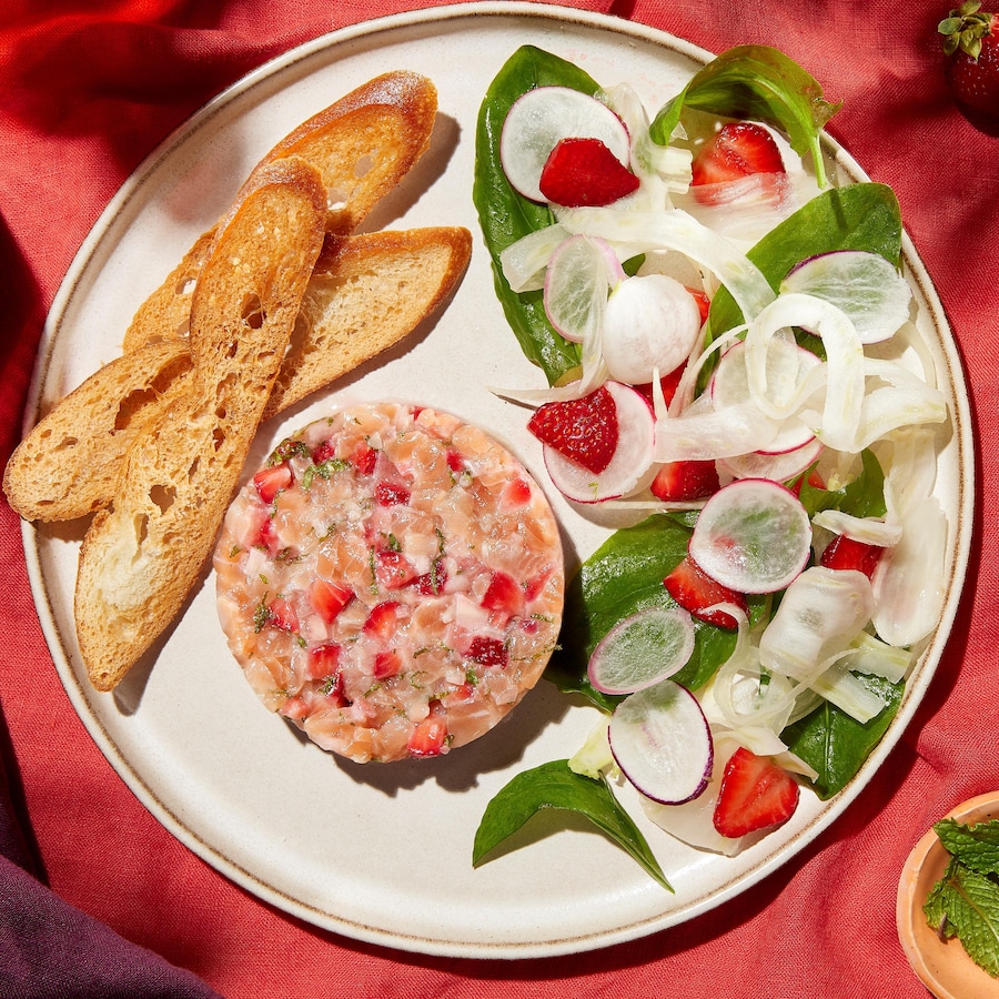Une assiette contenant du tartare de truite à la fraise, une salade de fenouil et oseille, ainsi que des croûtons.