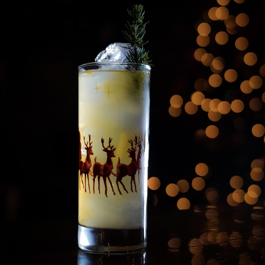 Un cocktail Tom Collins à l’érable et au gingembre dans un verre avec des glaçons et une branche de sapin.