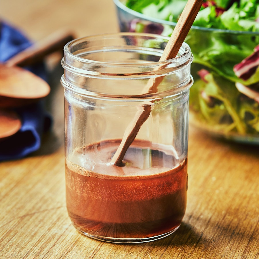 Bocal en verre contenant la vinaigrette et une cuillère de bois.